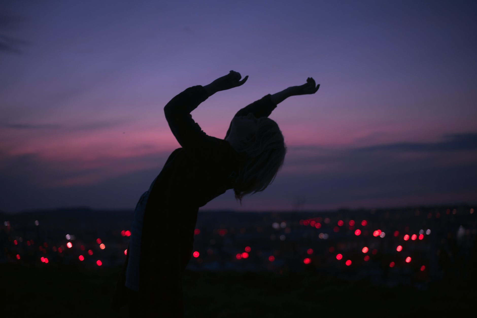 anonymous woman dancing on roof against night city