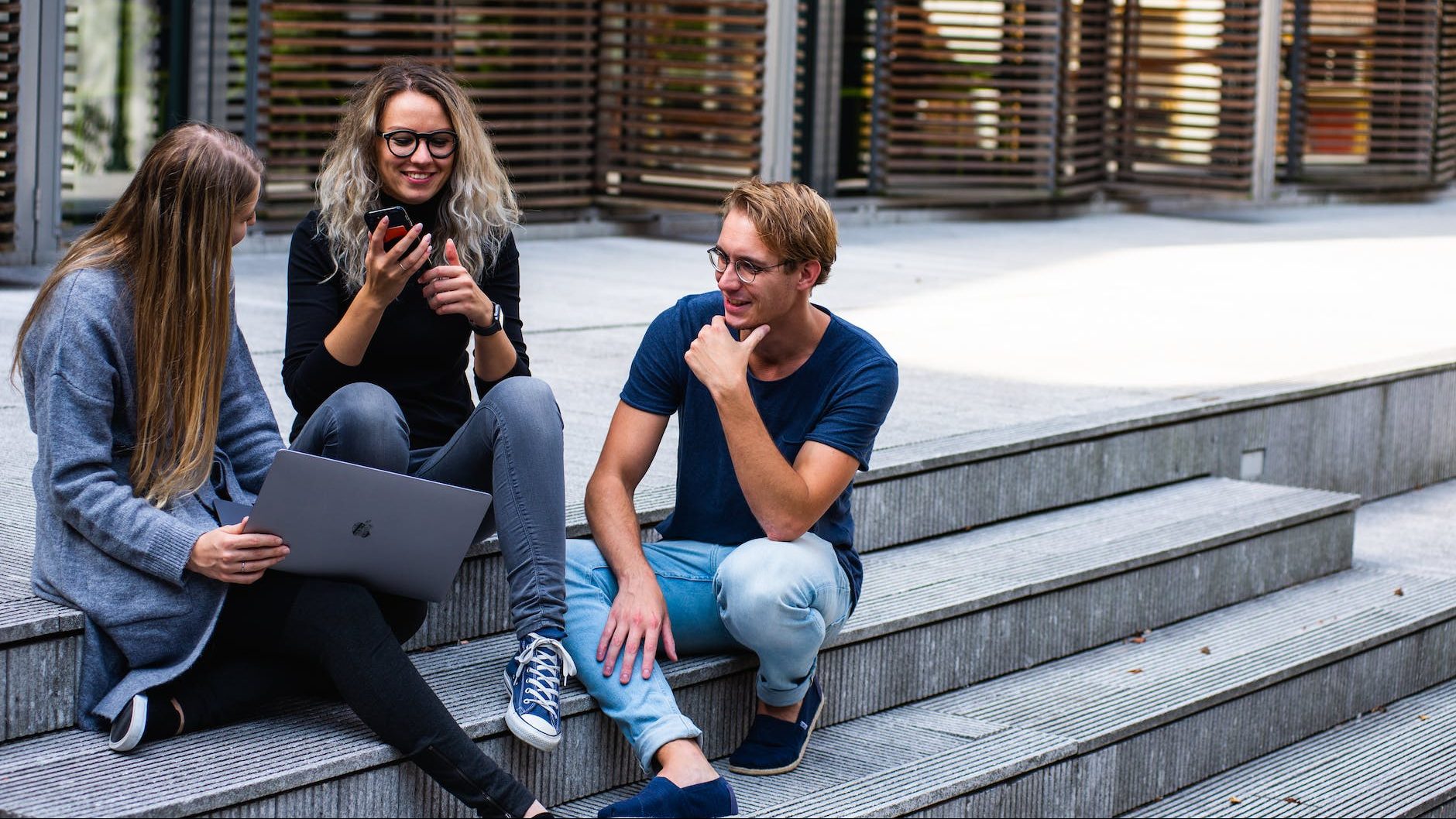 three persons sitting on the stairs talking with each other